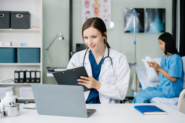 Young female doctor in white medical uniform using laptop and tablet talking video conference call at desk,Doctor sitting at desk