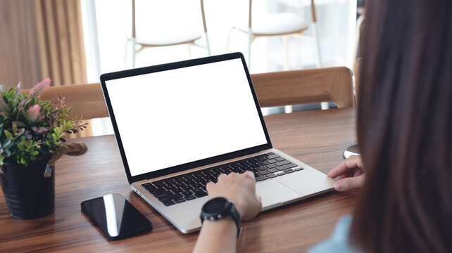Mockup blank white screen laptop computer. Business woman using and searching the information on laptop with empty screen on wooden table in modern loft cafe. Back view