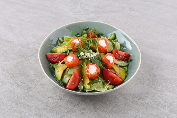 Salmon salad with green leaves, avocado and tomato on black stone background. Top view with copy space.