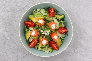 Salmon salad with green leaves, avocado and tomato on black stone background. Top view with copy space.