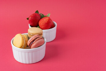 Macarons in white ramekins on a red background. Baking with strawberries. Dessert close-up with copy space. French breakfast