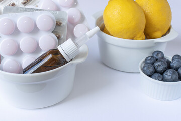 Drops in a warm glass bottle lie next to the packages of tablets. White background. Close-up with copy space