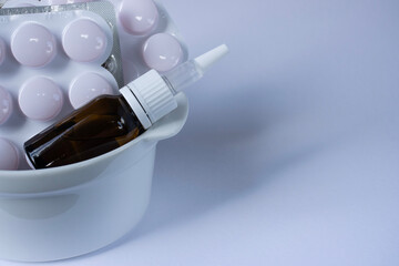 Drops in a warm glass bottle lie next to the packages of tablets. White background. Close-up with copy space