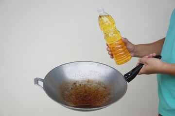 Close up chef holds frying pan which contain old oil or used cooking oil and bottle of vegetable...