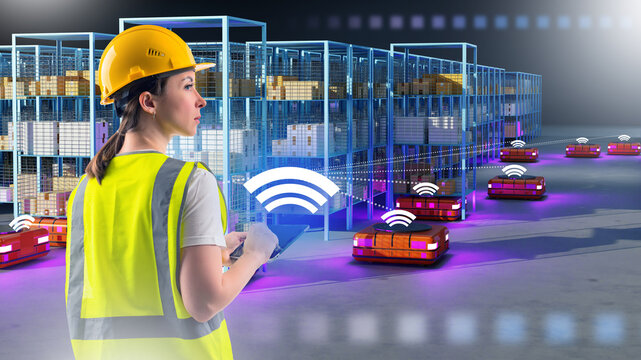 Woman controls warehouse robots. Automated guided vehicles. Girl monitors work warehouse robots. Storekeeper in yellow uniform. Warehouse automation. Robots in storage hangar. AGV for moving racks