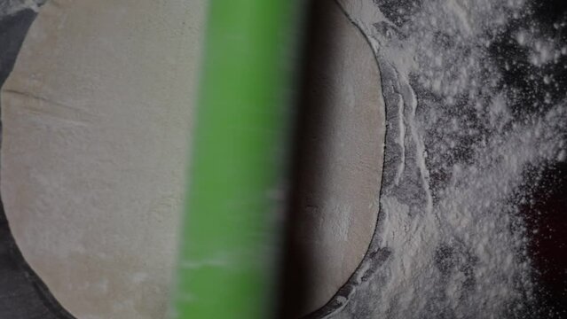 Close uo shot a dough being rolled by a green rollin pin