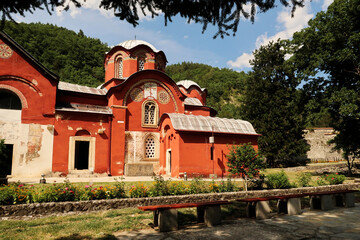 View onto the front facade and roof, domes, cupolas of the bright red Church Complex inside the courtyard, garden of the Patriarchate of Pec Monastery with a bench in the foreground, Peja, Kosovo