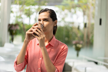 Young woman enjoying a refreshing drink iced coffee at cafe smiling and looking at her beverage...