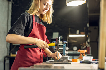 A jeweler uses a hammer to hammer out a unique ring design with a metal stamp. Craft in a jewelry workshop