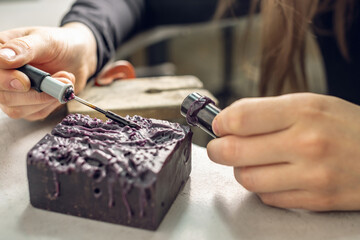 A female jeweler constructs a unique ring design using wax melting. Craft in a jewelry workshop