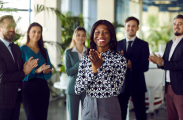 Portrait of a happy African American businesswoman celebrating success and applauding, surrounded...