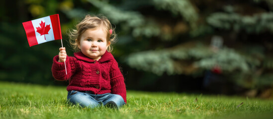 cute toddler sits on the grass, holding Canadian flag. Dressed in red sweater and jeans, child smiles softly celebrating Canada Day outdoors. promoting national pride, family celebrations