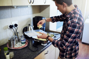 Cooking, student and man with cheese for meal prep, nutrition and melting shredded ingredients for lunch. Diet, food and home chef at kitchen counter with pan, recipe and roasting for dinner