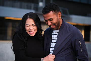 Latin man and woman are laughing in a city. Happy couple hanging out.