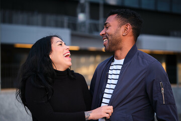 Latin man and woman are laughing in a city. Happy couple hanging out.
