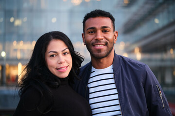 Latin woman and man are smiling at the camera in a city. Scene is happy and friendly.