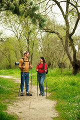 Fototapeta premium A man and a woman are walking in a forest, both carrying backpacks. They are both smiling, doing hiking or trekking.