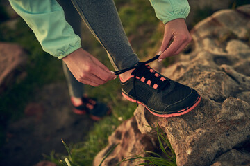 Person, hands and tying shoe with rock of hiker for morning walk or trekking on outdoor mountain....