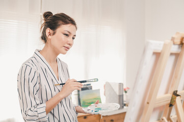 Portrait photo of young beautiful Asian woman artist painting water color art picture in indoor studio.