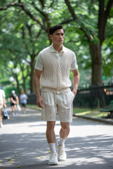 Obraz premium Young Asian man in casual summer attire walking in a city park.