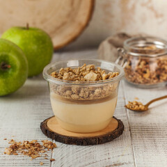 A delectable milk-based dessert topped with apple granola, presented in a clear plastic cup