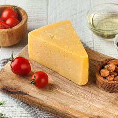 A wedge of semi-hard cheese displayed on a rustic wooden cutting board, accented with fresh cherry...
