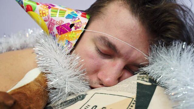 Man dressed in festive cap with tinsel sleeps deeply after party. Overwhelmed man finds solace in slumber after Christmas festivities