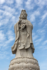 Obraz premium Giant white Guan Yin statue at Guanyin Bodhisattva Pavilion in Kanchanaburi, Thailand. Beautiful Chinese goddess sculpture against blue sky, famous religious landmark for tourism.
