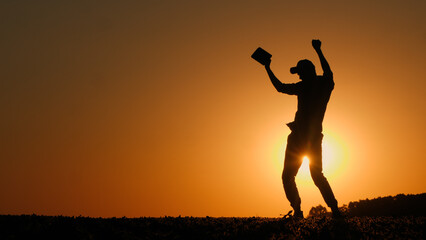 A man with a tablet in his hand dances a cheerful dance in a field at sunset