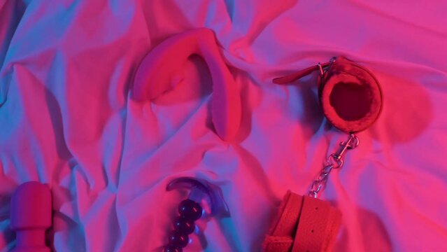 set of woman sex toys for masturbation and orgasm on a sheet on the bed. Female vibrator, vacuum stimulator, butt plug and BDSM handcuffs in neon lighting