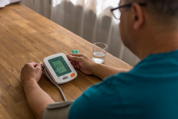 Seniory man checks blood pressure with monitor on upper arm in room