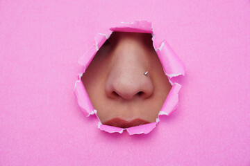A woman's nose and mouth are visible through pink torn paper