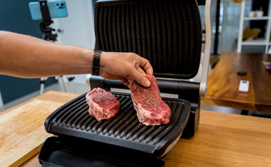 Chef at the kitchen preparing beef steaks on the home electric grill