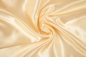 Golden cream color satin cloth arranged in the shape of a swirl, abstract textured backdrop