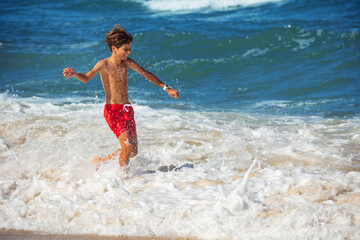 Boy joyfully running on refreshing beach waves, wear red shorts