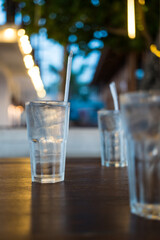 A glass of water with ice and white straw on the wood table at restaurant