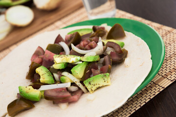 Salad of black tomatoes, avocado and onions in Italian tortilla on green plate