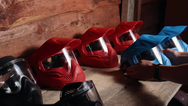 Paintball combat, Paintball equipment, Shelf arrangement. Lineup red and blue paintball masks is neatly organized on wooden shelf, and prior to commencing game, player selects mask from shelf.