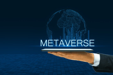 A hand holding a tablet projecting a holographic globe with the word METAVERSE set against a dark...