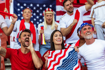 American sport fans cheering at the stadium with flags and other equipment.