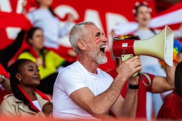 Sport fans are cheering for their team at the stadium on the match. The cheer leader uses a...