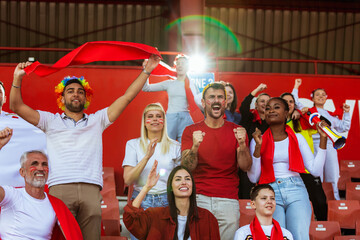 Fototapeta premium Sport fans are cheering for their team at the stadium on the match in red colors.