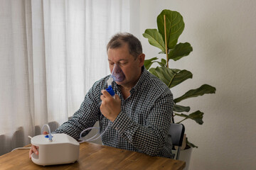 Elderly man sitting on a table and using a nebulizer mist at home
