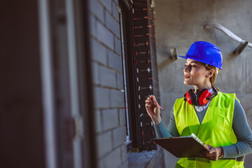 Portrait of successful woman constructor wearing yellow helmet and safety yellow vest. Portrait of...