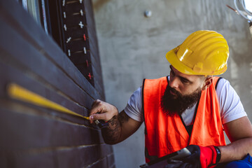 Construction worker using measuring tape to measure dimensions of the wall.