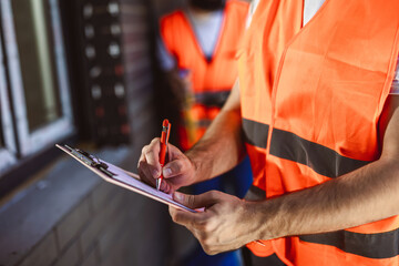 Construction site manager standing  wearing safety vest  and writing on paper.