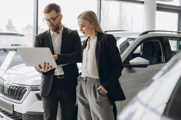 A male salesman showing something on a laptop to a female client buying a car inside a car...