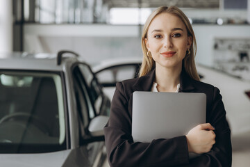 Pensive stylish businesswoman manager in suit holding laptop computer, standing near car at car...