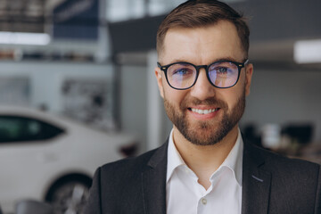 Close-up portrait of bearded businessman in glasses smiling and suit at car dealership