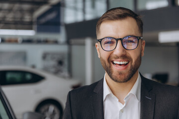 Close-up portrait of bearded businessman in glasses smiling and suit at car dealership